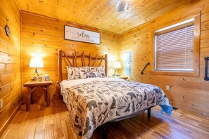 Ein Zimmer einer Holzhütte mit einem Bett, zwei Nachttischlampen, einem Fenster mit Jalousien und einem Schild an der Wand.
