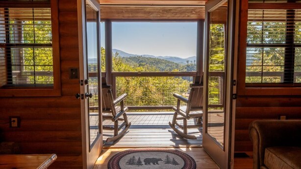 A wooden cabin interior with a balcony, rocking chairs, and a view of a forested mountain range. - Ridge Vista (Gatlinburg)