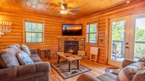 A log cabin interior with a fireplace, a television, and a sofa. - Ridge Vista (Gatlinburg)