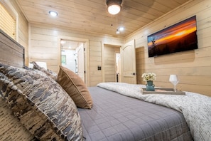 A cozy bedroom with a bed, pillows, a bedside table with a vase and glass, and a painting on the wall. - Valley Cove (Sevierville)