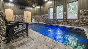 An indoor swimming pool with stone walls, wooden doors, and a bench. - Valley Cove (Sevierville)