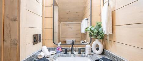 A bathroom with wooden walls, a marble sink, a mirror, a towel rack, and a potted plant.