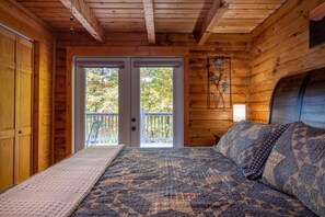 A wooden cabin bedroom with a bed, a bench, and a view of trees through a door. - Lasting Memories (Sevierville)