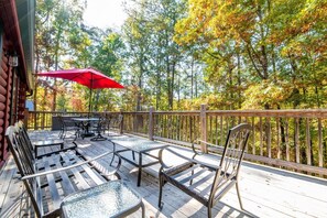 A wooden deck with outdoor furniture, a red umbrella, and a view of trees. - Lasting Memories (Sevierville)