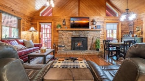 A log cabin interior with a stone fireplace, leather furniture, and a dining area. - Lasting Memories (Sevierville)
