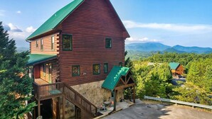 A log cabin with a green roof, a stone foundation, and a balcony. - Windows to Heaven (Sevierville)