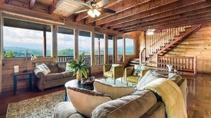 A spacious room with a large window, a ceiling fan, a staircase, and a cozy seating area. - Windows to Heaven (Sevierville)