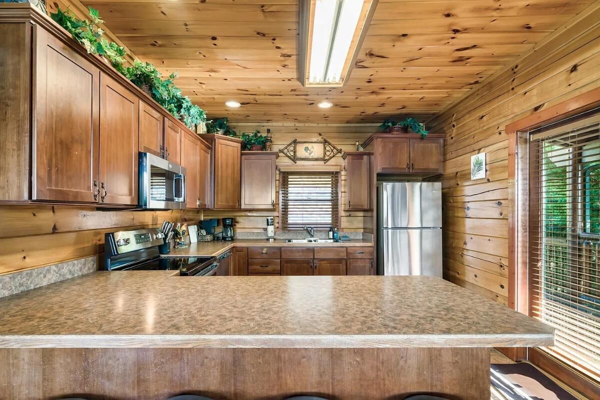 A kitchen with wooden cabinets, a central island, stainless steel appliances, and a window with blinds.