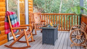 A wooden deck with rocking chairs, a table with a fire feature, and a wheel chair. - Three Little Bears 2 (Gatlinburg)