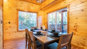 A wooden cabin with a dining table set for four, large windows, and a view of the outdoors. - Three Little Bears 2 (Gatlinburg)