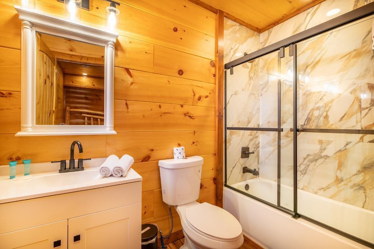 A wooden interior with a bathroom including a sink, toilet, and glass-enclosed shower.