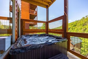 Een houten terras met een jacuzzi, een balkon en uitzicht op een bebost gebied.