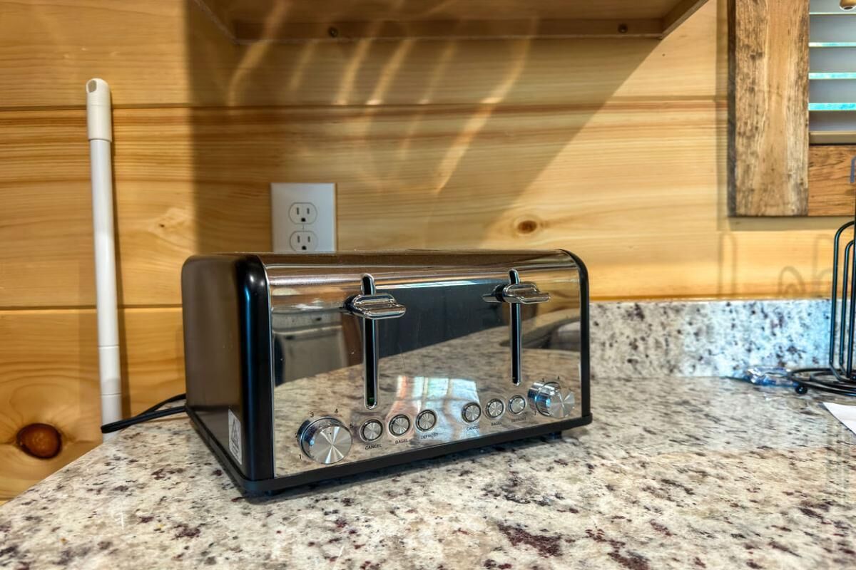 A kitchen with a toaster on a granite countertop, wooden walls, and a visible electrical outlet.