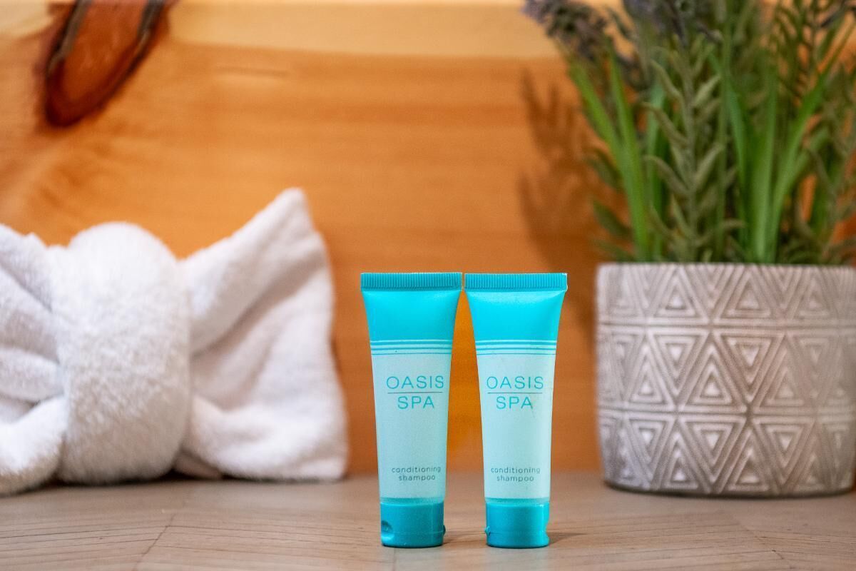 Two tubes of OASIS SPA conditioning shampoo, a white towel, and a potted plant on a wooden surface.