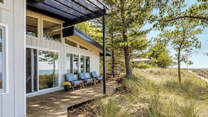 A modern house with a covered porch, large windows, and a view of the beach. - The Beach Bungalow | Coastal Vibe | Private Beach! (West Olive)