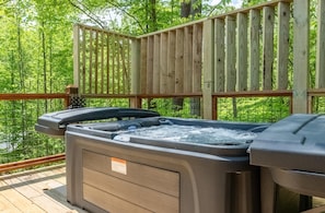 Ein Whirlpool auf einer Holzterrasse, mit Holzzaun und Grünpflanzen im Hintergrund.