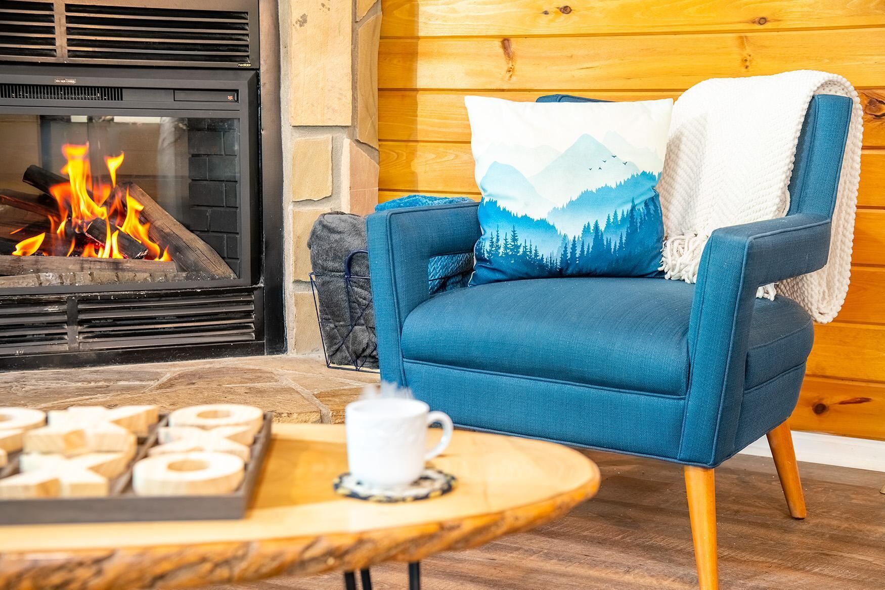 A cozy room with a blue armchair, a fireplace, and a table with a cup and pastries.