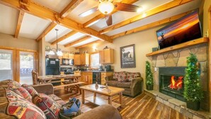 A cozy living room with a fireplace, wooden beams, a dining area, and a kitchen. - Cozy Bear Cove 2 (Pigeon Forge)