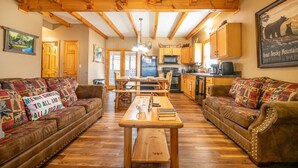 A cozy living room with wooden beams, a dining table, and two sofas with festive cushions. - Cozy Bear Cove 2 (Pigeon Forge)
