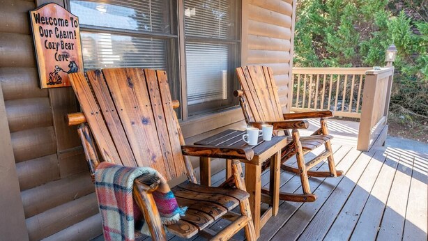 A cabin with wooden chairs and a table on the porch, a welcome sign, and a view of trees. - Cozy Bear Cove 2 (Pigeon Forge)