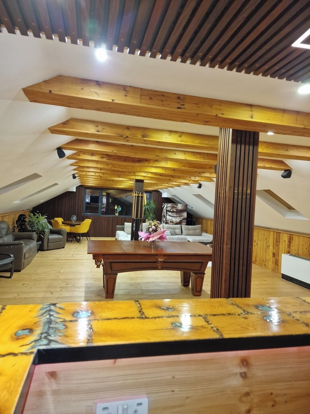 Un ampio loft con soffitto alto, travi in legno a vista, un tavolo centrale in legno e un'accogliente area salotto con divano e poltrone.