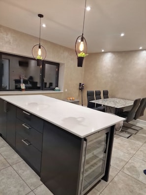 Una cucina moderna con una grande isola, mobili scuri e illuminazione a sospensione.