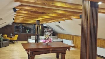 A loft-style room with wooden beams, a dining table, sofas, and a large window.