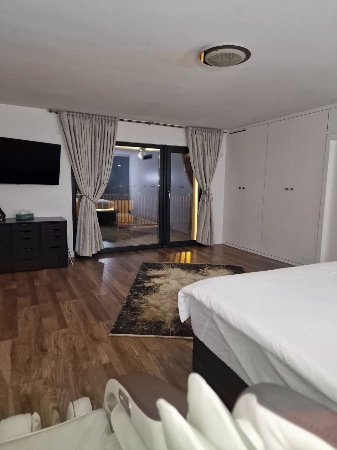 A bedroom with a bed, a desk, a chair, a TV, a wardrobe, and a balcony with a view.