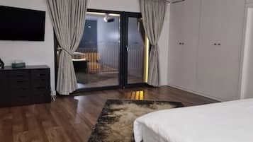 A bedroom with a bed, a desk, a chair, a TV, a wardrobe, and a balcony with a view.