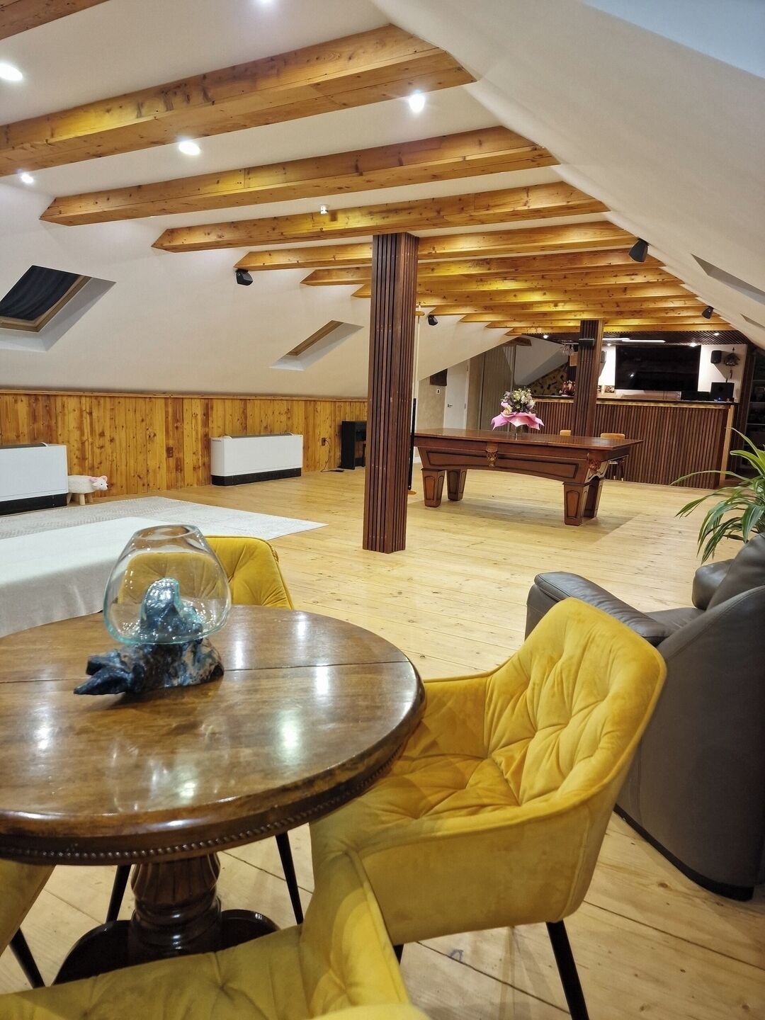 Un'ampia stanza con soffitto in legno, un tavolo da pranzo con sedie, un divano e una televisione.