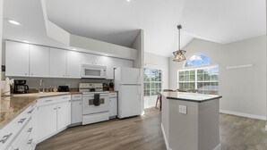Una cocina moderna con armarios blancos, microondas, refrigerador y piso de madera.