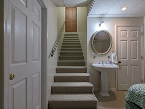 A staircase leading to a landing, a white door, a wall-mounted mirror, and a pedestal sink. - Llyn Blaen House at Lake Junaluska (Lake Junaluska)
