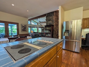 A modern kitchen with a stone accent wall, a large island with a built-in stove, and a stainless steel refrigerator. - Llyn Blaen House at Lake Junaluska (Lake Junaluska)