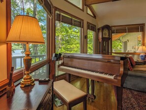A grand piano in a well-lit room with large windows, a bench, and a lamp. - Llyn Blaen House at Lake Junaluska (Lake Junaluska)