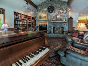 A living room with a grand piano, a fireplace, a stone wall, and a bookshelf. - Llyn Blaen House at Lake Junaluska (Lake Junaluska)