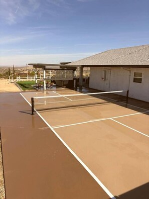 A tennis court with a net, a covered seating area, and a building in the background. - Ultimate Retreat|Pool~Spa~Pickleball~GameRoom~BBQ (Twentynine Palms)