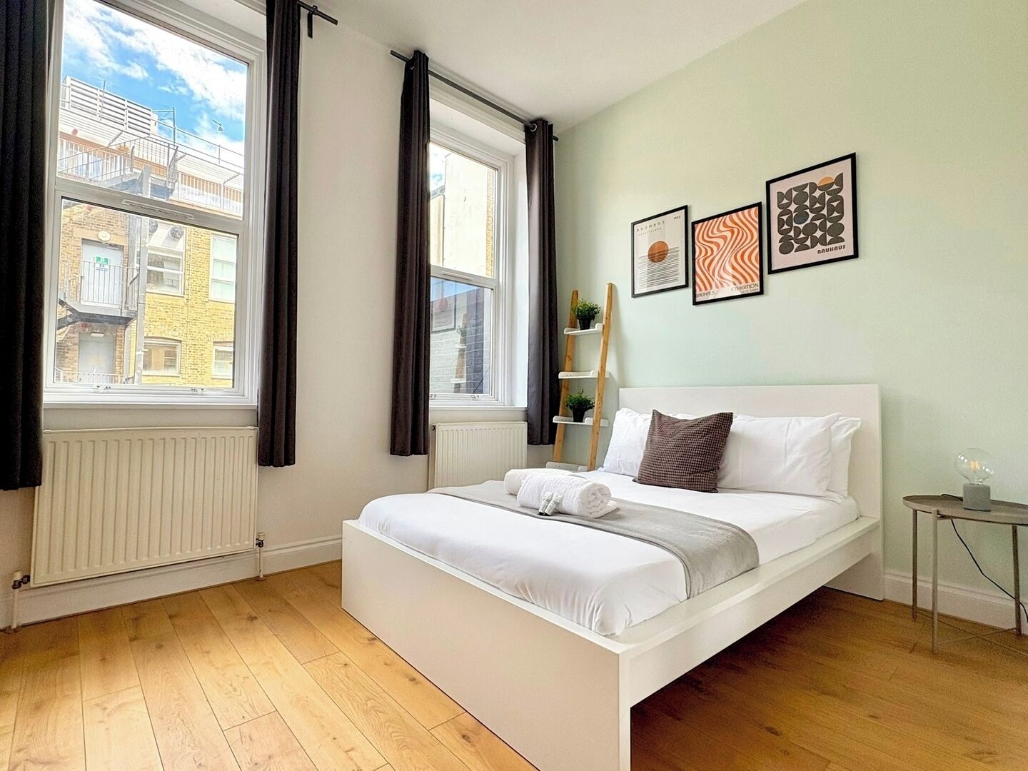 A bedroom with a bed, windows, and artwork on the wall.