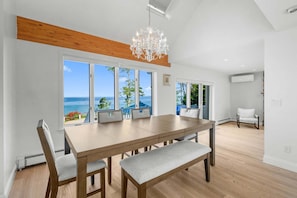 A dining area with a wooden table, grey upholstered chairs, and a chandelier. - Ocean's Edge with pool, hot tub & beach access (Plymouth)