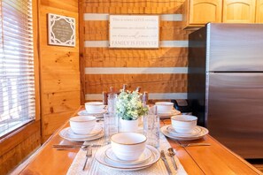 A dining table set with white plates and bowls, a vase with flowers, and a stainless steel refrigerator in a wooden kitchen. - Living Waters Lodge (Sevierville)