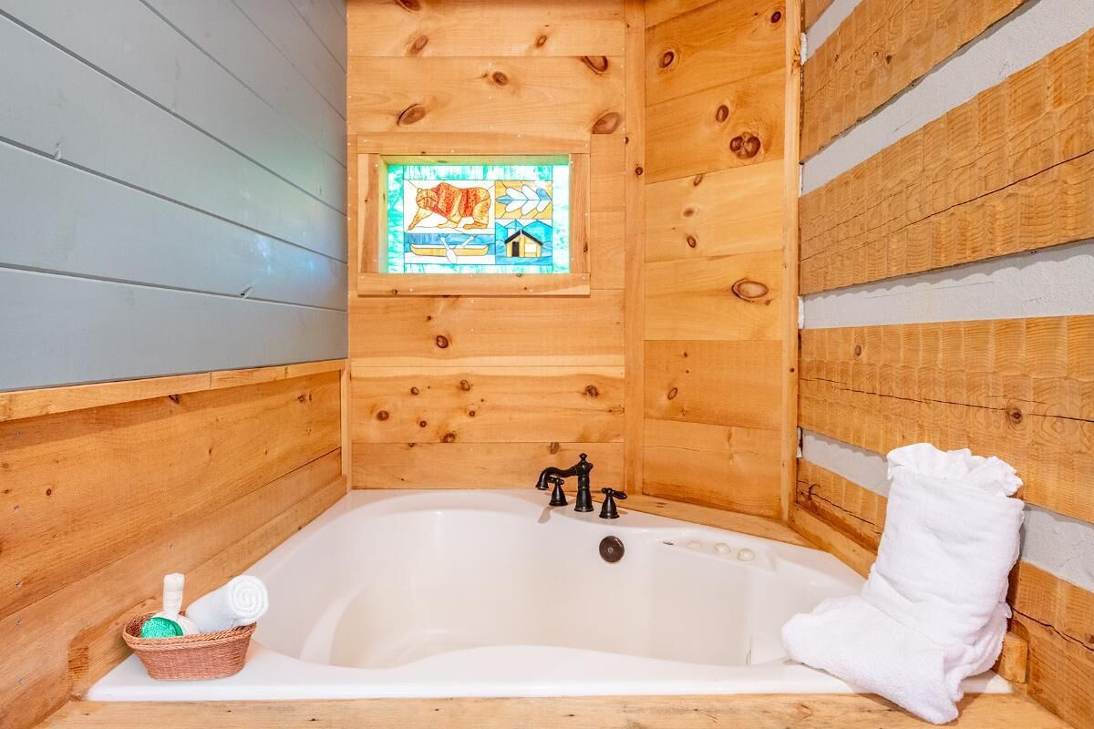 Una cabana de fusta amb interior de panells de fusta, una banyera blanca, una finestra amb un disseny de vitrall i una cistella amb articles de bany.