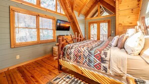 Un dormitorio de cabaña de madera con cama, vigas de madera y televisor en la pared.