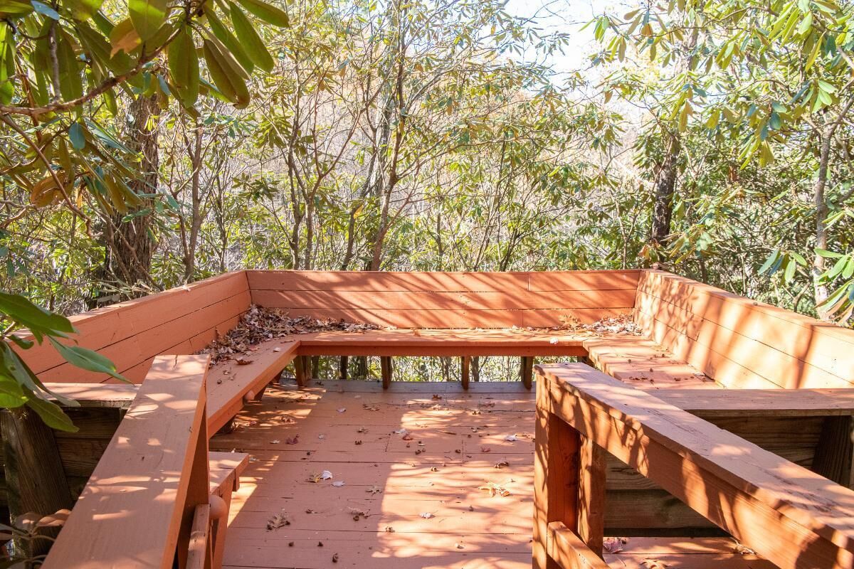 Une terrasse en bois, agrémentée de bancs et d’une table, entourée d’arbres.