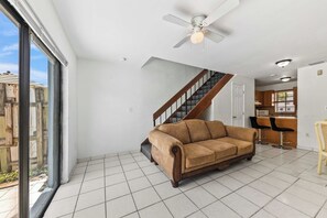 A spacious living area with a large window, a ceiling fan, a staircase, and a kitchen area. - 3BR • Step-Free Entry • 2 Free Parking Spots (Miami)