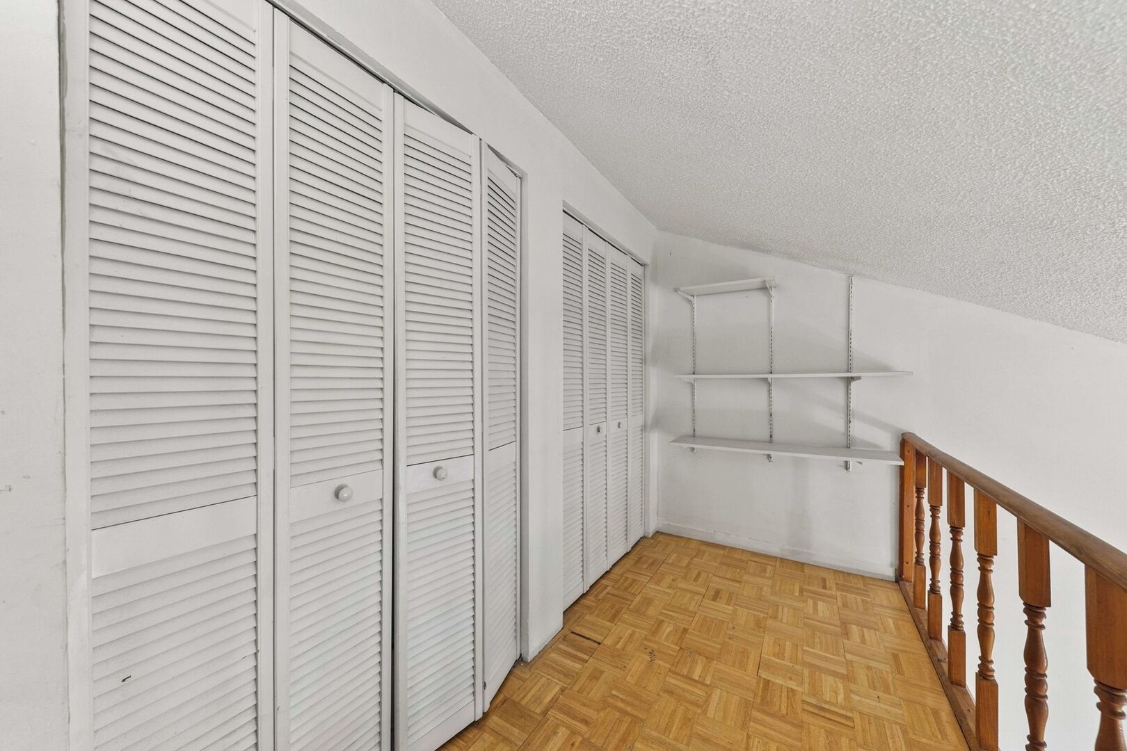 A room with a wooden floor, white walls, and a wooden staircase railing.