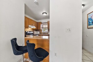 A kitchen with wooden cabinets, a microwave, and a stove. There are two black chairs with white stitching. - 3BR • Step-Free Entry • 2 Free Parking Spots (Miami)