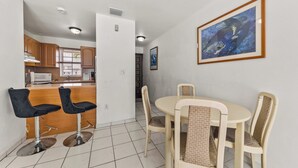 Comedor con una mesa redonda y cuatro sillas, una cocina al fondo y un cuadro en la pared.