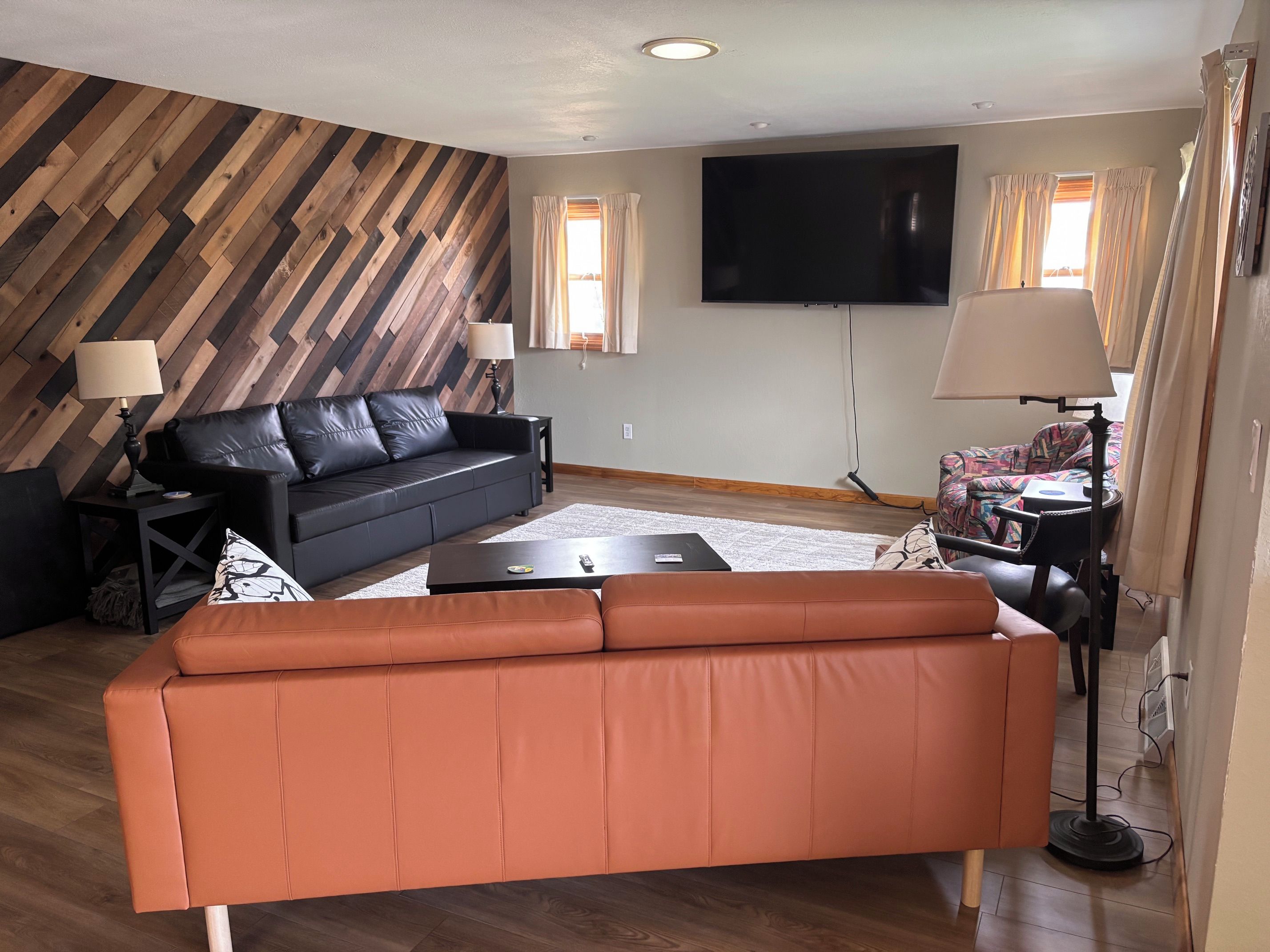A living room with a black leather sofa, a brown leather sofa, a flat-screen TV, and a patterned armchair.