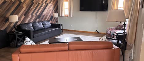 A living room with a black leather sofa, a brown leather sofa, a flat-screen TV, and a patterned armchair.