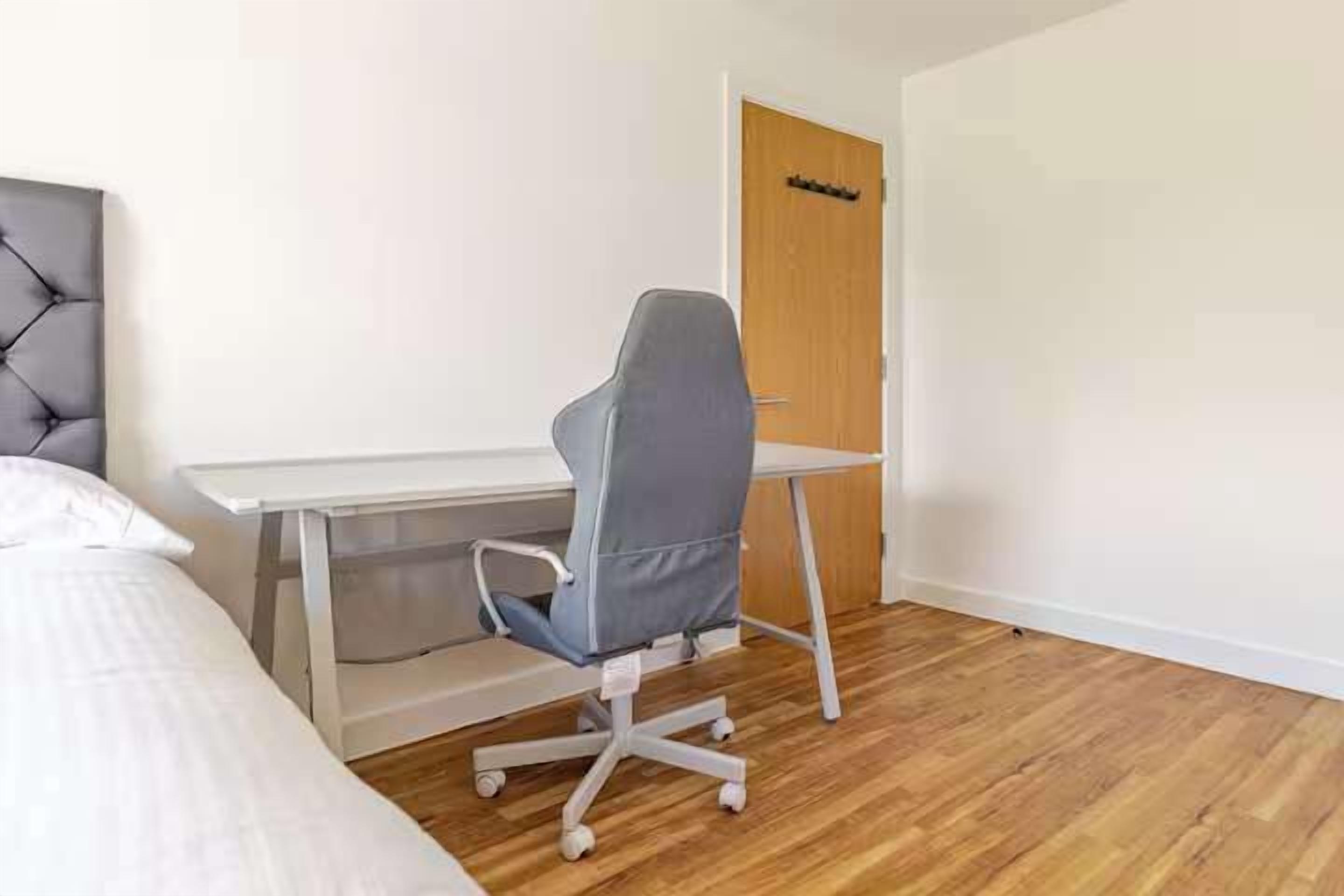A bedroom with a bed, a desk, a chair, and a door.