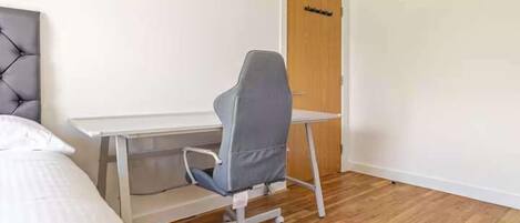A bedroom with a bed, a desk, a chair, and a door.